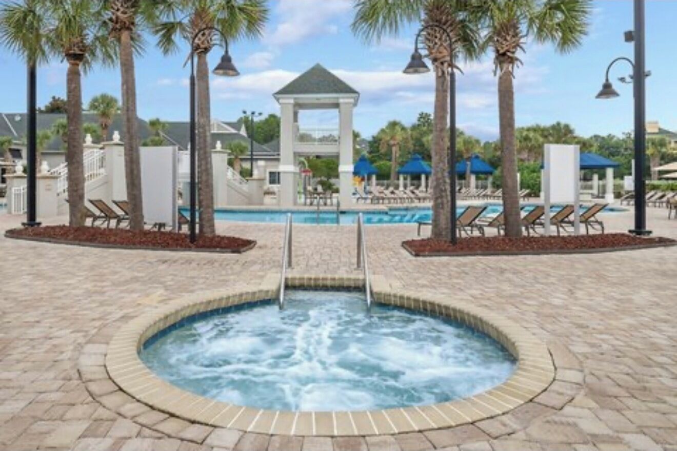 A hot tub surrounded by lounge chairs and palm trees, with a gazebo in the background.