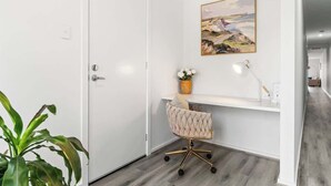 A modern office space with a white door, a desk with a cushioned chair, a vase with flowers, a lamp, and a painting on the wall. - Stylish 3BR Stay Close to Tea Tree Plaza (Modbury)