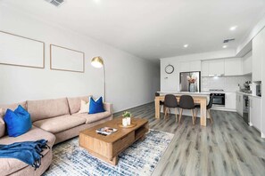 A modern living room with a sofa, coffee table, and a dining area with chairs. - Stylish 3BR Stay Close to Tea Tree Plaza (Modbury)