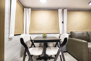 Un rincón comedor pequeño con una mesa y cuatro sillas, un cuenco pequeño de aperitivos y un sofá.
