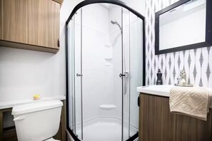 Ein modernes Badezimmer mit einer Glaskabine zur Dusche, einer weißen Toilette und Holzschränken.
