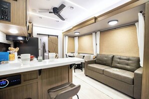 Une cuisine compacte au design moderne, comprenant un four encastré, une machine à café et une horloge numérique. Un coin salon avec un canapé et une table à manger est également prévu.