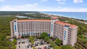 Um hotel grande, com vários andares e telhado curvo, rodeado por um parque de estacionamento e vegetação exuberante.