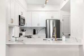 Uma cozinha moderna com armários brancos, eletrodomésticos de aço inoxidável e bancada de mármore.