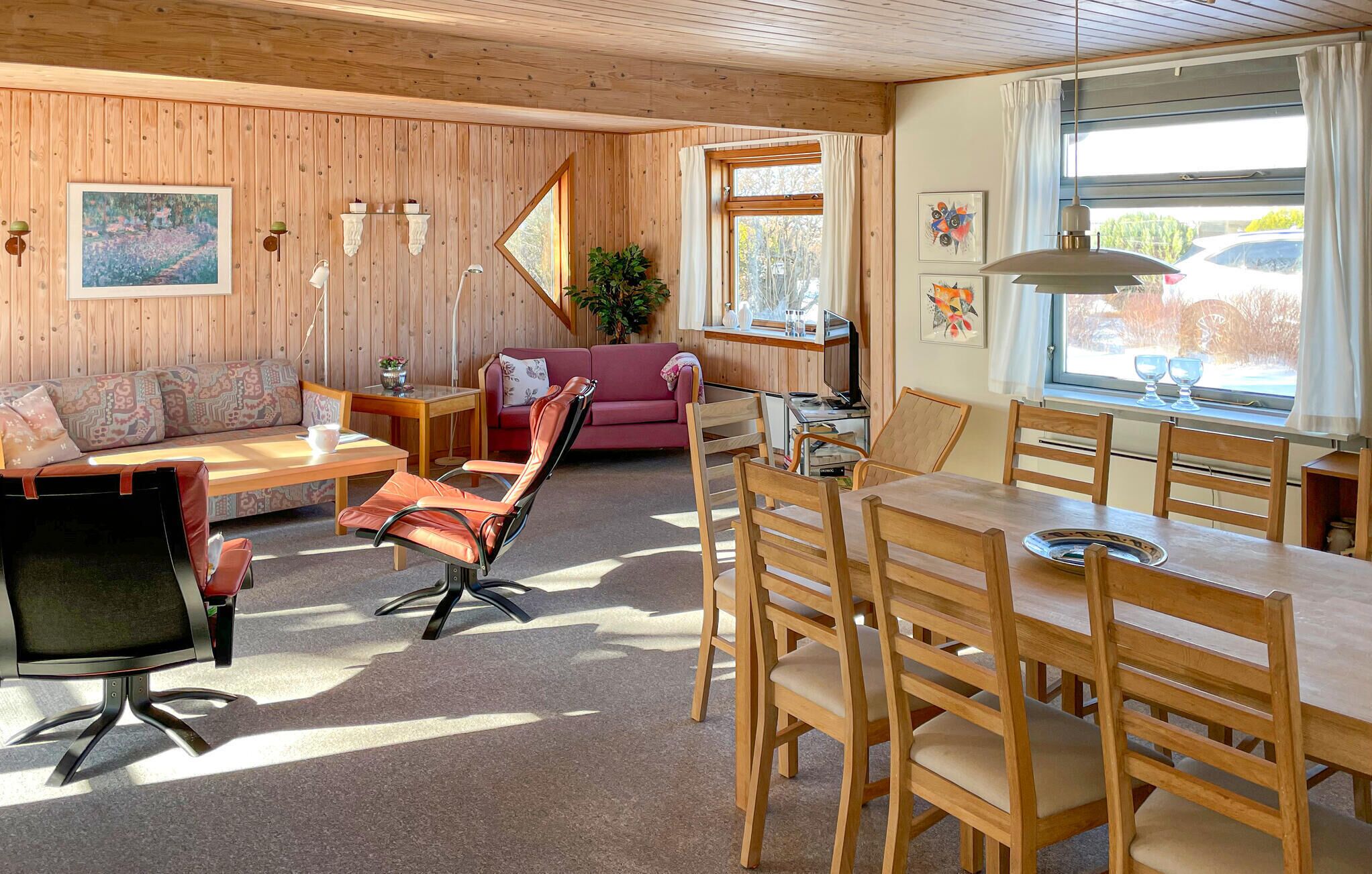 Una sala de estar acogedora con un sofá, un sillón rosa, una mesa de comedor con sillas, un televisor y una ventana con cortinas.