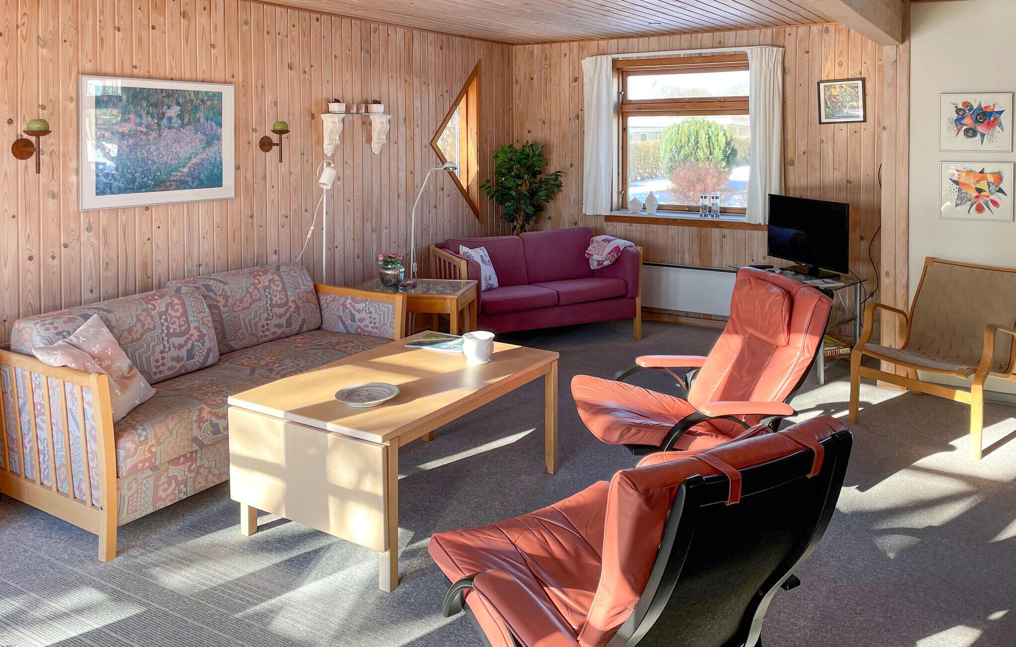 Un salon chaleureux avec un décor intérieur en bois, un canapé, un fauteuil rouge, une table basse et un téléviseur.