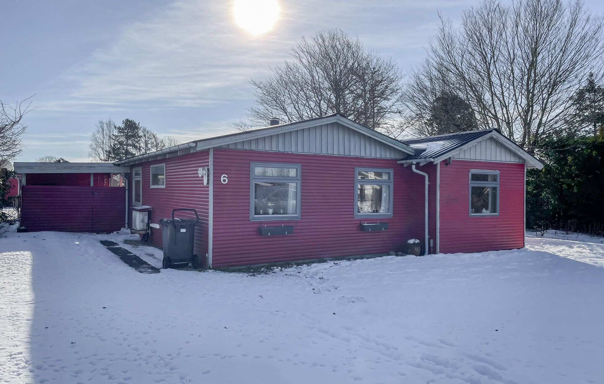 Ein rotes, eingeschossiges Haus mit Garage, Nummer 6, in verschneiter Landschaft.