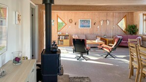 Una sala de estar acogedora con chimenea de leña, un sofá, sillones, una estantería y un comedor.