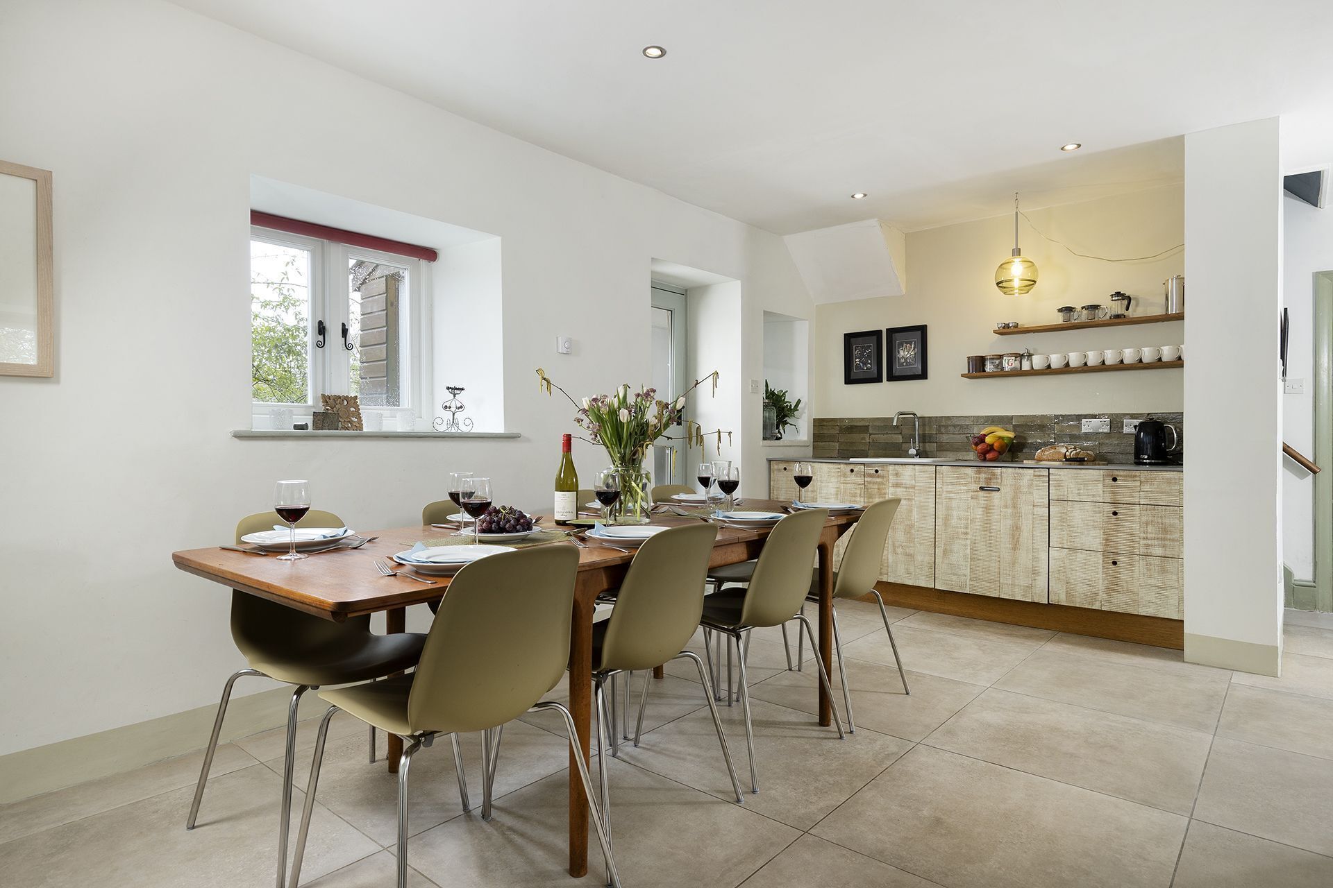 A modern kitchen with a dining area, featuring a large island, pendant lighting, and a view of the outdoors.