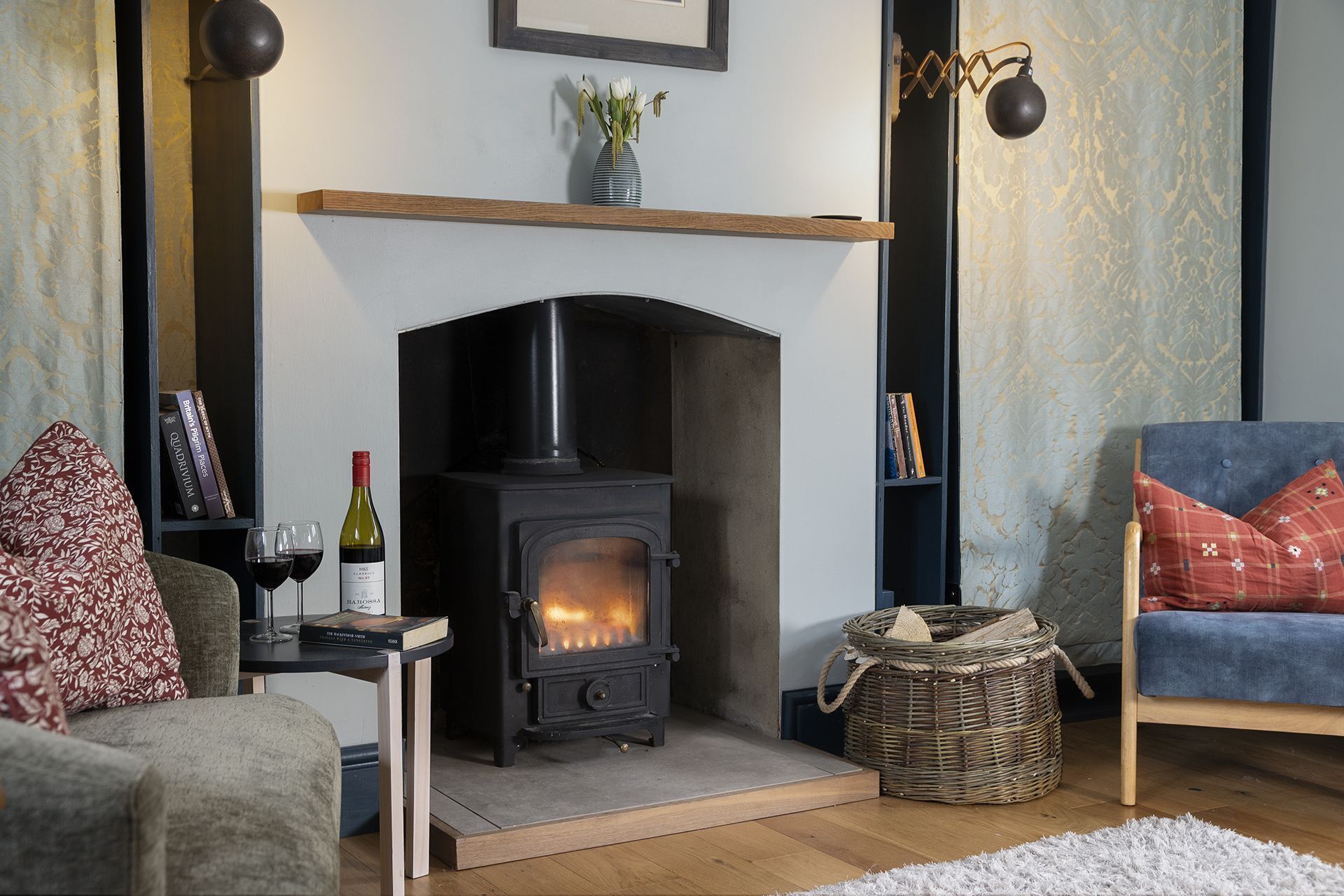 A cozy living room with a fireplace, a bookshelf, a wicker basket, and a comfortable chair.