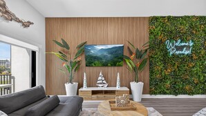 Un salon moderne doté d’un grand téléviseur à écran plat, d’un canapé, d’une table basse et d’un mur décoratif orné d’une inscription : « Bienvenue au paradis ».
