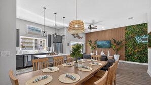 Une cuisine moderne dotée d’appareils électroménagers en acier inoxydable, un coin repas avec une table et des chaises en bois, et un espace de vie avec un téléviseur et un mur végétal.