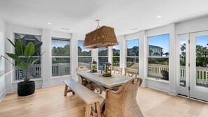 A spacious room with a large dining table, wicker furniture, and a hanging light fixture. - Modern Coastal Beach Home! Across from Beach Access w/Ocean Views & a Huge Yard w/Private Pool! (Isle Of Palms)
