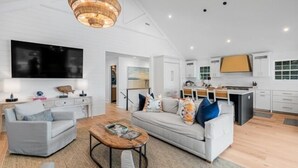 A modern living room with a sofa, coffee table, and TV. - Modern Coastal Beach Home! Across from Beach Access w/Ocean Views & a Huge Yard w/Private Pool! (Isle Of Palms)
