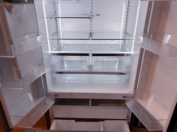 Un refrigerador moderno y vacío con varios estantes y cajones transparentes.
