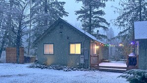 En træhytte med to vinduer, en veranda og snækkedække jord.