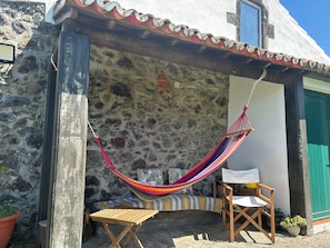 A stone building with a hammock, a wooden chair, and a small table. - Charming country home (Santo António de Nordestinho)