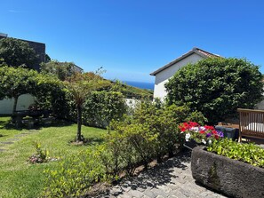 A garden with a stone bench, a variety of plants, and a view of the sea. - Charming country home (Santo António de Nordestinho)