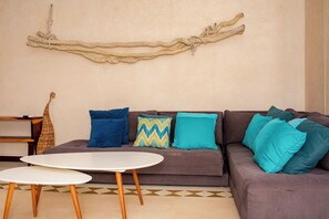 Un salon avec un canapé marron, une table blanche et une corde décorative accrochée au mur.