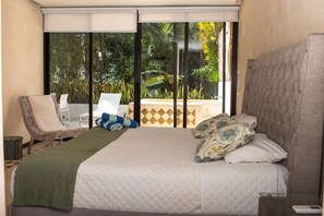 Une chambre avec un grand lit, une chaise et une vue sur la verdure grâce à une porte coulissante.