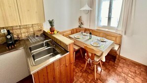 A compact kitchen with wooden cabinets, a sink, and a dining area with a table set for two. - Casa Zanetti a Le Prese Appartamento "Bernina" by Interhome (Le Prese)