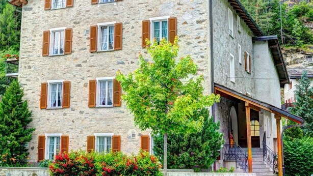 A stone building with multiple windows and a balcony, surrounded by greenery and trees. - Casa Zanetti a Le Prese Appartamento "Bernina" by Interhome (Le Prese)