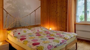 A bedroom with wooden walls, a bed with a colorful floral bedspread, a large abstract painting, and a window with curtains. - Casa Zanetti a Le Prese Appartamento "Bernina" by Interhome (Le Prese)