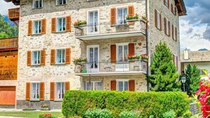 A multi-story stone building with wooden shutters, balconies with flower boxes, and a well-maintained hedge in front. - Casa Zanetti a Le Prese Appartamento "Bernina" by Interhome (Le Prese)