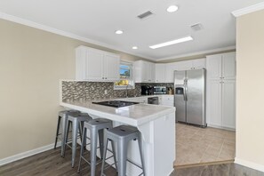 A modern kitchen with white cabinets, a large island with bar stools, a stainless steel refrigerator, and a microwave. - NEW LISTING! A License to Chill, 4BD/3BA gulf front w/panoramic views, private pool, pet friendly! (Port St. Joe)
