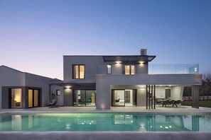 Une maison moderne à deux étages, avec une piscine en premier plan.