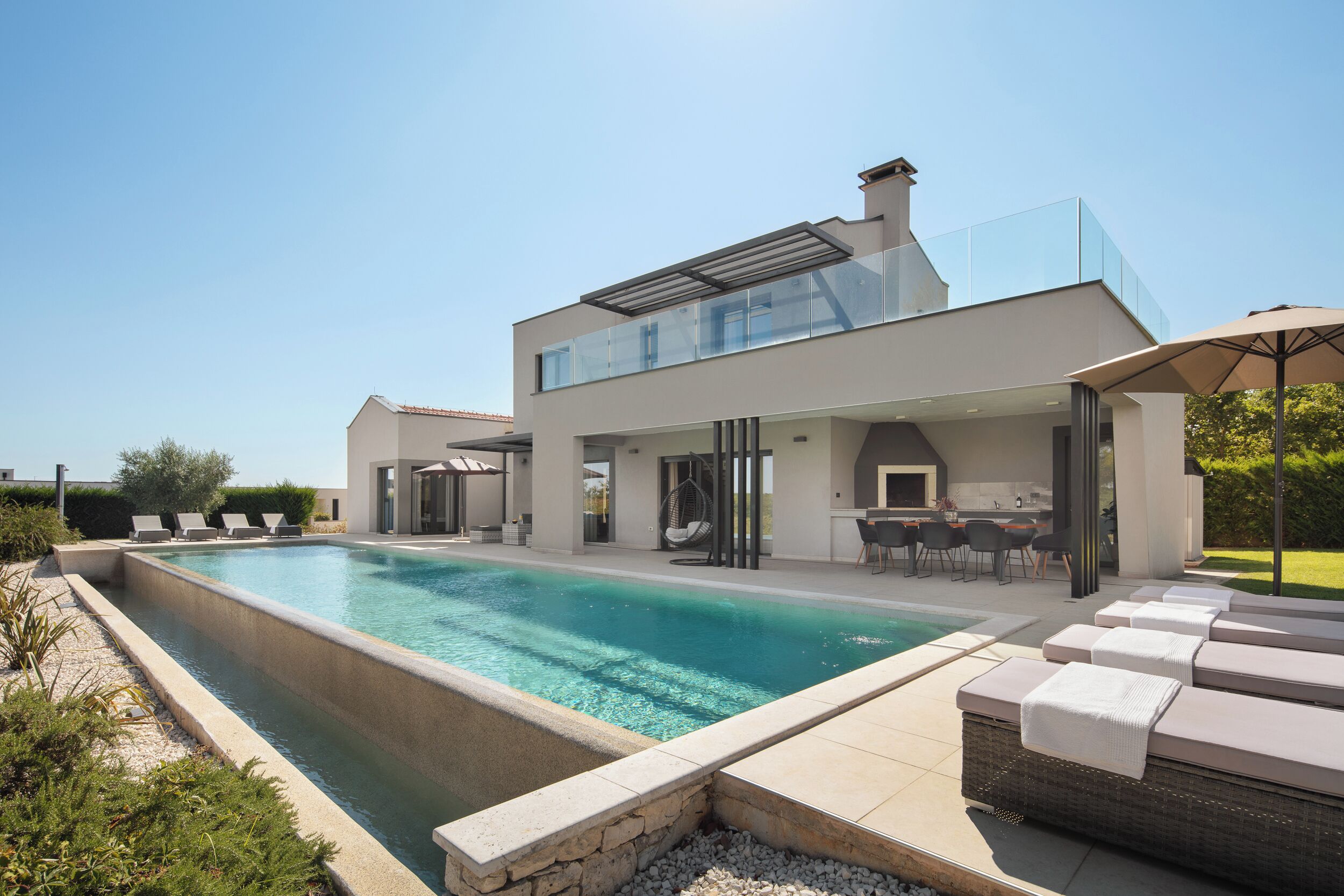 Una casa moderna con piscina, mobiliario de exterior y un porche cubierto.