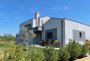 Une maison moderne à deux étages, dotée d’un toit plat, d’une cheminée et d’un petit porche.