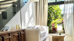 Una sala de estar moderna con una escalera, un sofá, una mesita de centro y vistas al verdor exterior.