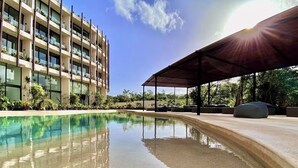 Una piscina de borde curvo, rodeada por una zona de estar cubierta y un edificio con balcones.