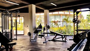 Un gimnasio con diverso equipo de ejercicio, ventanas amplias y vista a zonas verdes.