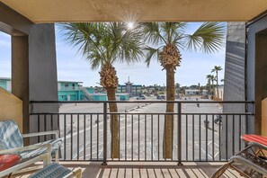 A balcony with a view of a parking lot and palm trees, featuring a chair and a table. - Beachside Studio at Hawaiian Inn w/ Pools & Beach Access (Daytona Beach Shores)