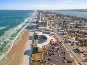 An aerial view of a coastal city with a beachfront hotel, parking lot, and surrounding residential area. - Beachside Studio at Hawaiian Inn w/ Pools & Beach Access (Daytona Beach Shores)