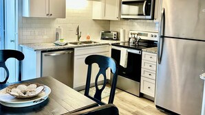 A modern kitchen with white cabinets, stainless steel appliances, a dining table with chairs, and a ceiling fan. - Sunny Beach & Lakefront Condo Steps to the sand, beautifully renovated! (North Myrtle Beach)