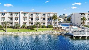 A multi-story hotel with balconies, a swimming pool, and a rocky shoreline. - Sunny Beach & Lakefront Condo Steps to the sand, beautifully renovated! (North Myrtle Beach)