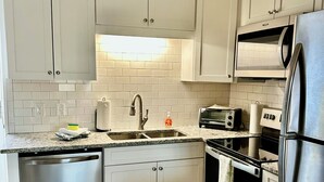 A modern kitchen with white cabinets, stainless steel appliances, a microwave, toaster, and dishwasher. - Sunny Beach & Lakefront Condo Steps to the sand, beautifully renovated! (North Myrtle Beach)