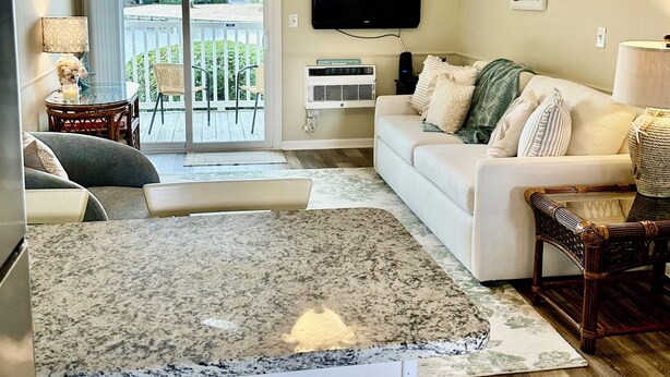 A living room with a white couch, a TV, a ceiling fan, and a view of a balcony. - Sunny Beach & Lakefront Condo Steps to the sand, beautifully renovated! (North Myrtle Beach)