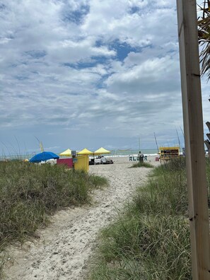 Un sendero arenoso que lleva a sombrillas de playa y un quiosco frente al mar.