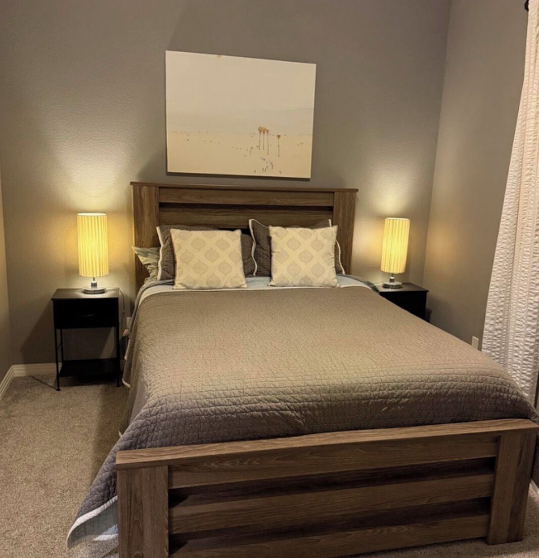 Une chambre à coucher avec un lit en bois, deux tables de chevet avec des lampes, une tête de lit et une œuvre d’art accrochée au mur.