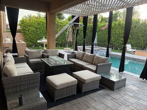 Ein überdachter Außenbereich mit Korbmöbeln und einem Tisch mit Glasplatte, mit Blick auf einen Swimmingpool.