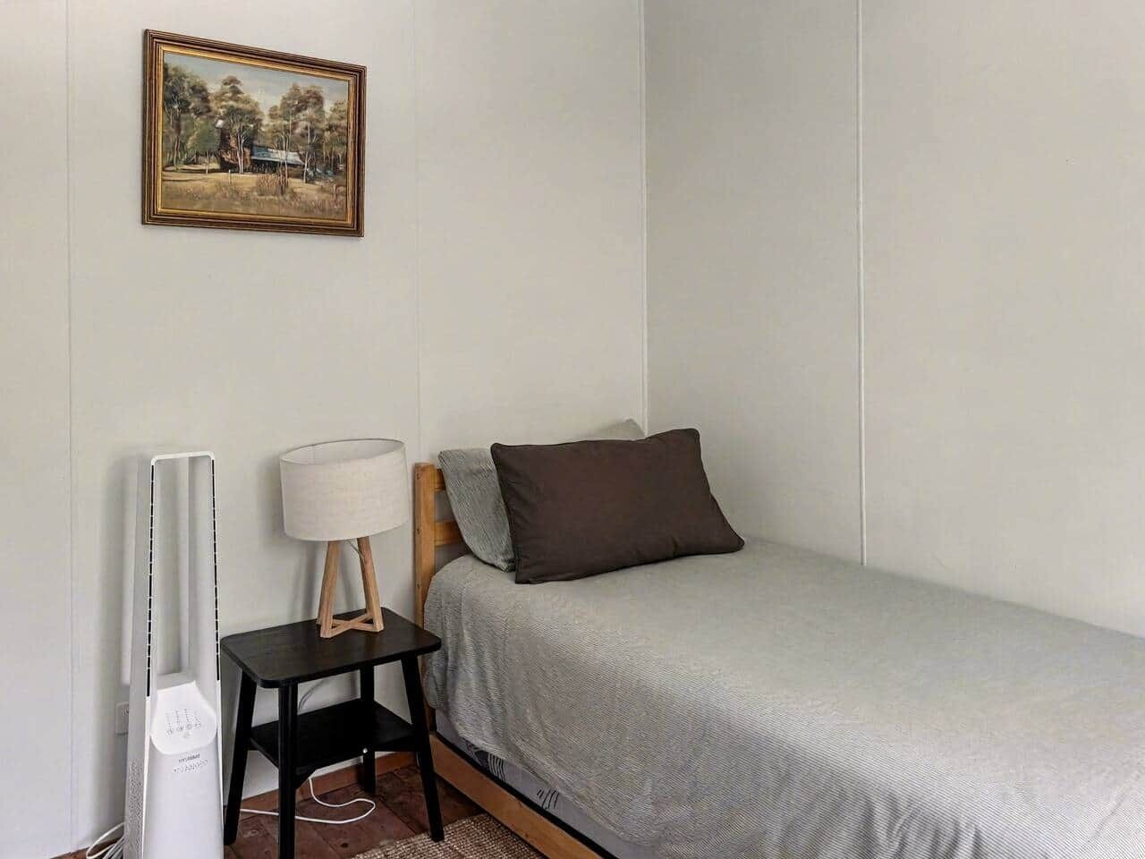 A bedroom with a single bed, a bedside table with a lamp, and a framed picture on the wall.