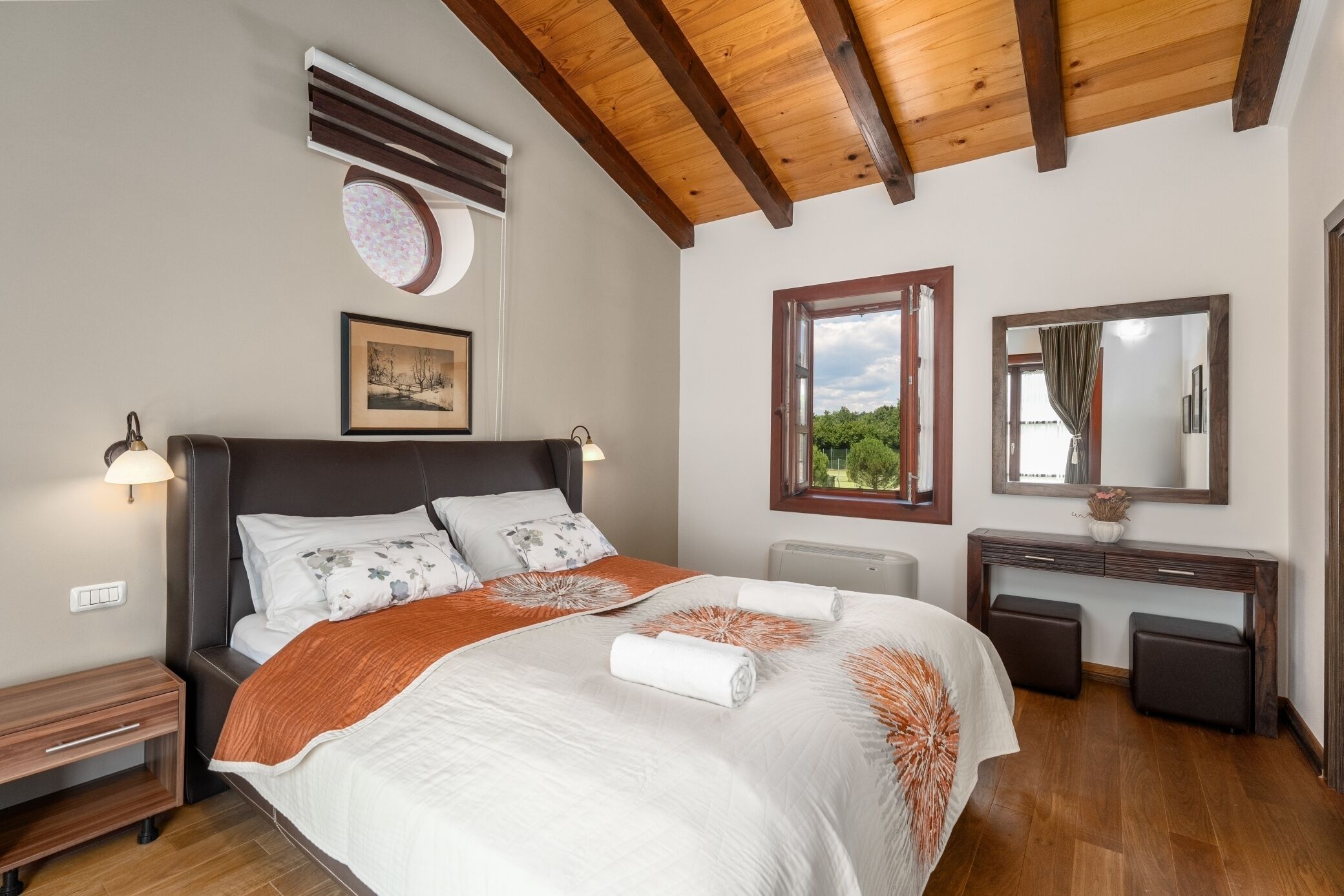 Un dormitorio con cama, mesitas de noche, cómoda, espejo y ventana con vistas.