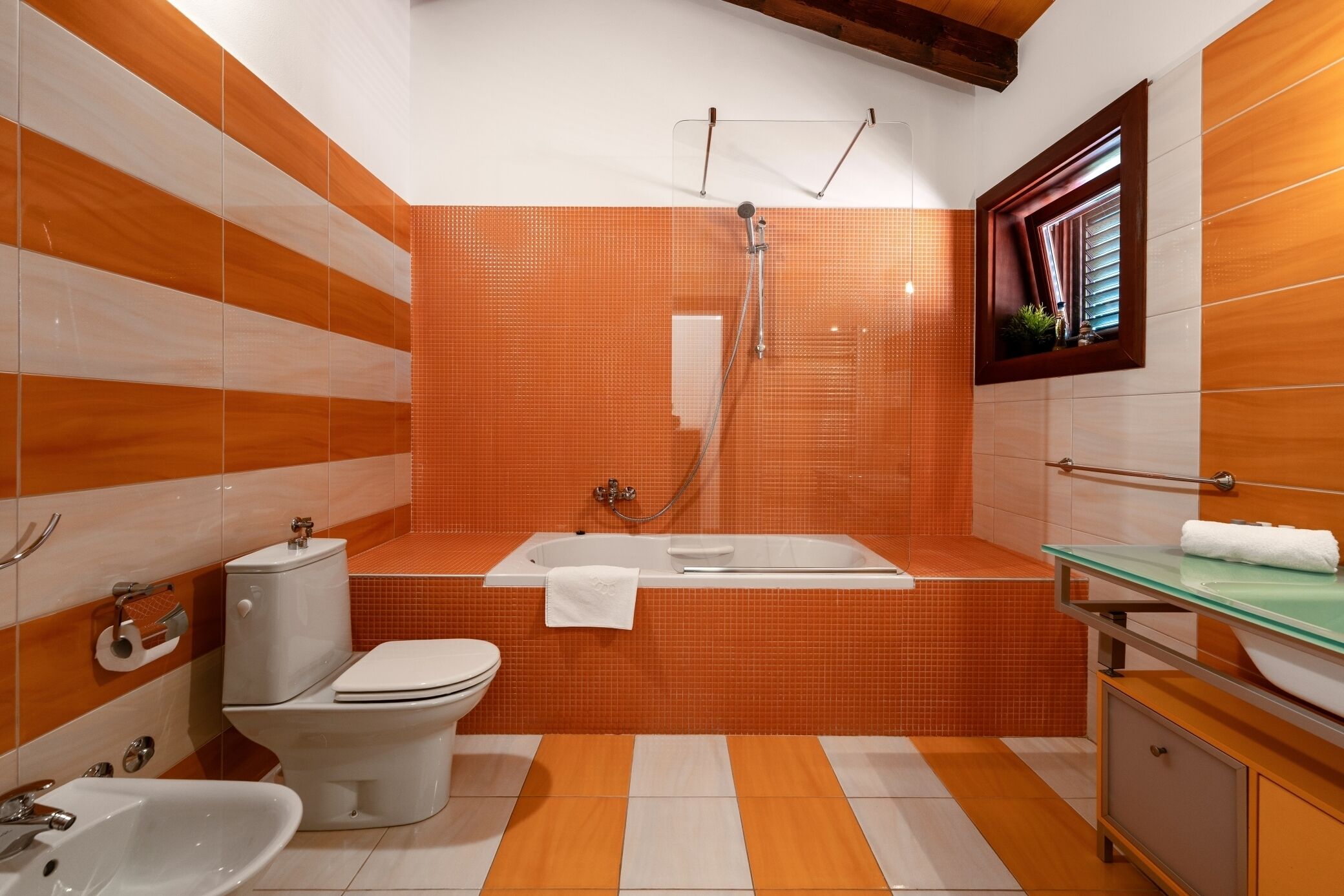Une salle de bain comprenant des toilettes, un bidet, un lavabo, une baignoire et une fenêtre avec des stores.