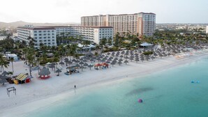 Ein Strandresort mit mehreren Hotelgebäuden, einem Sandstrand und zahlreichen Sonnenschirmen.