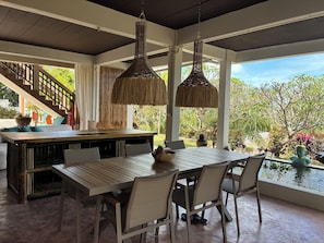 A spacious dining area with a long wooden table and white chairs, a staircase with a railing, and a view of lush greenery outside. - Villa Bleu Monkey Paradise (Chang Wat Surat Thani)