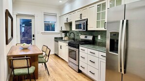 Une cuisine moderne avec des meubles blancs, un réfrigérateur en acier inoxydable, un four à micro-ondes et une cuisinière. On y trouve une table à manger avec des chaises et une fenêtre donnant sur un beau paysage.
